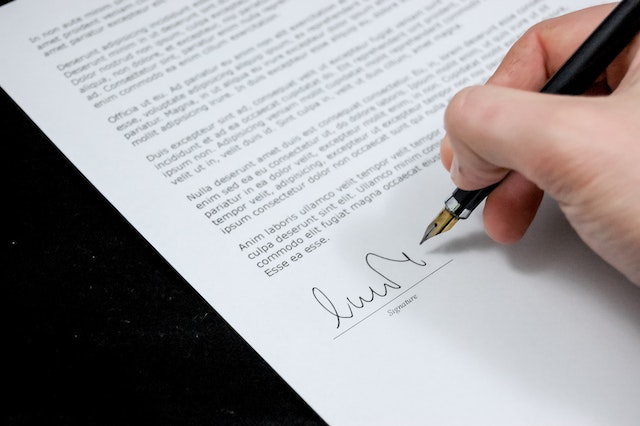 paper filled with text and a person's hand signing their signature with a fountain pain